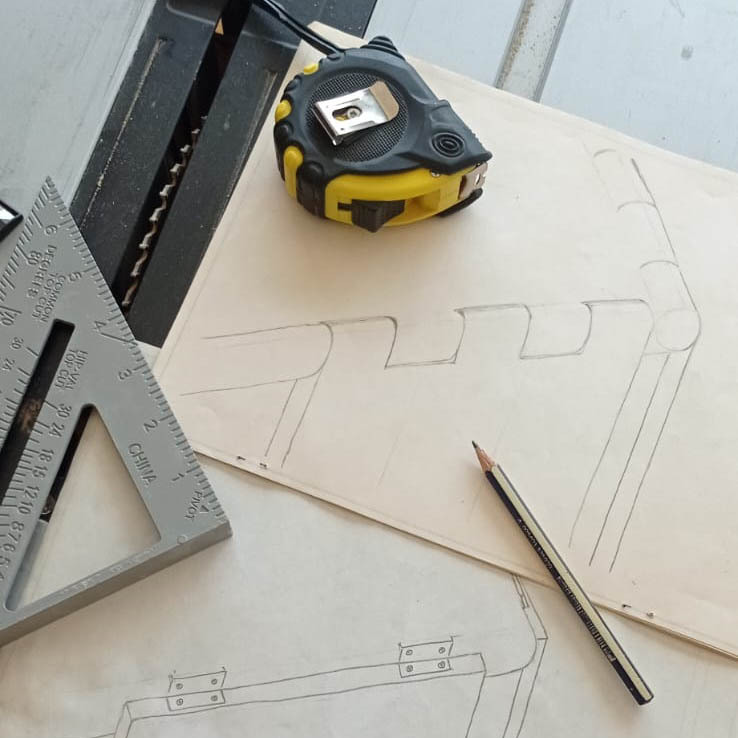 Foto de un plano de obra con una cinta métrica, un casco de obrero, un martillo y clavos